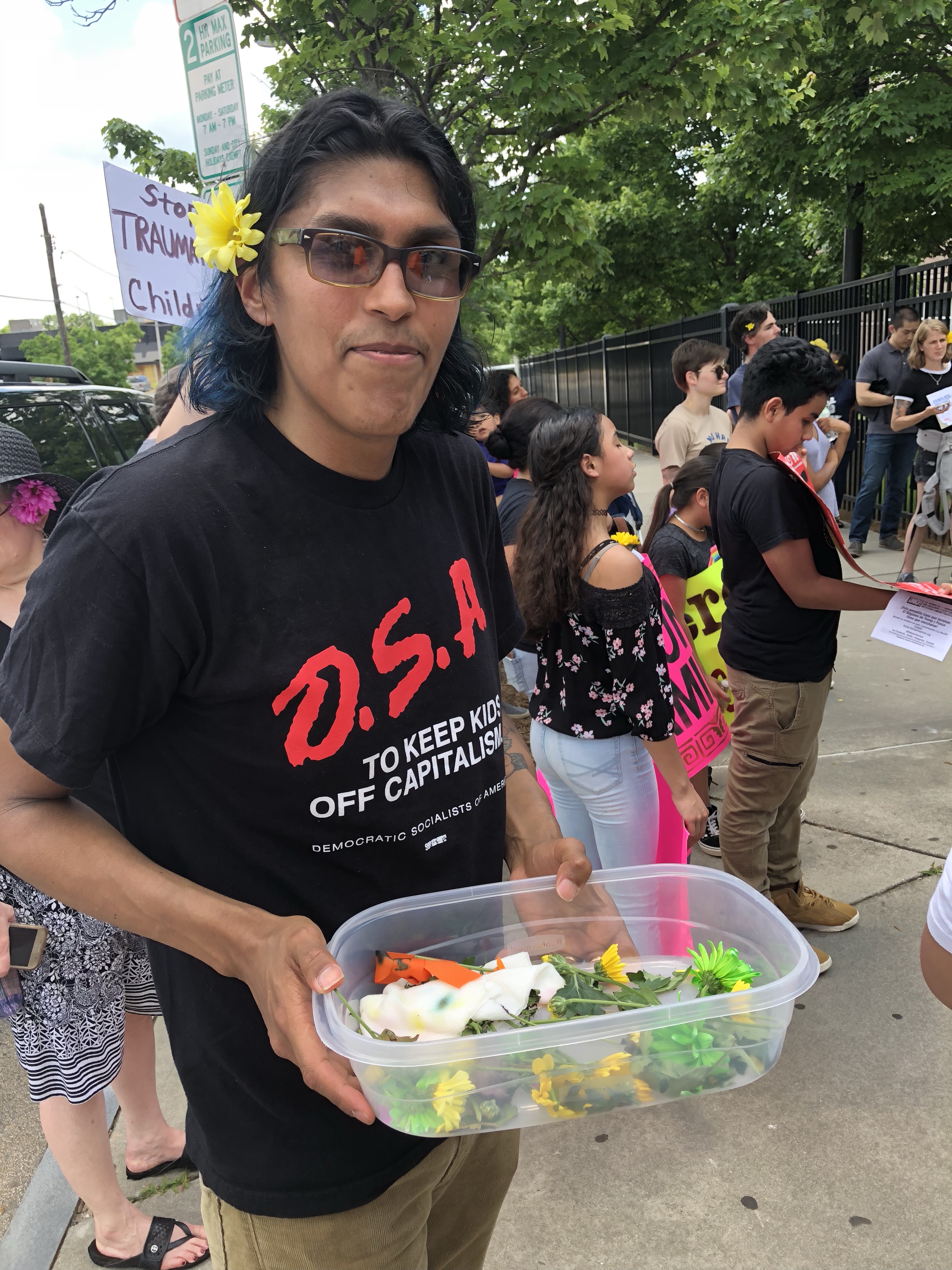 man with dark glasses holds a container of flowers at the rally