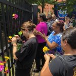 several people along with one woman in black shirt affixing a flower to a black fence