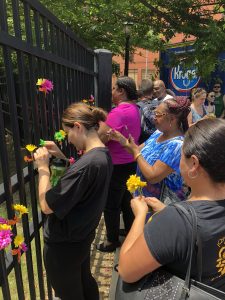 several people along with one woman in black shirt affixing a flower to a black fence