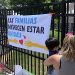 White sign on black fence saying families belong together