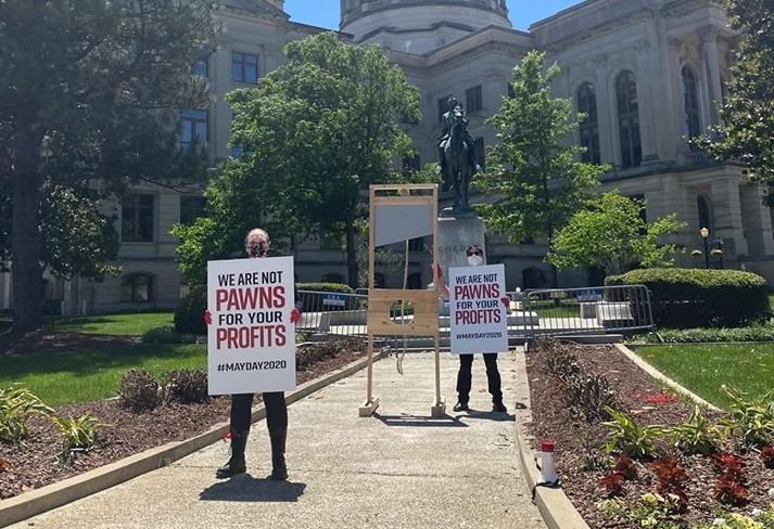 Atlanta DSA members hold up signs and display a DIY mock guillotine in front of the Georgia state capitol on May 1, 2020.